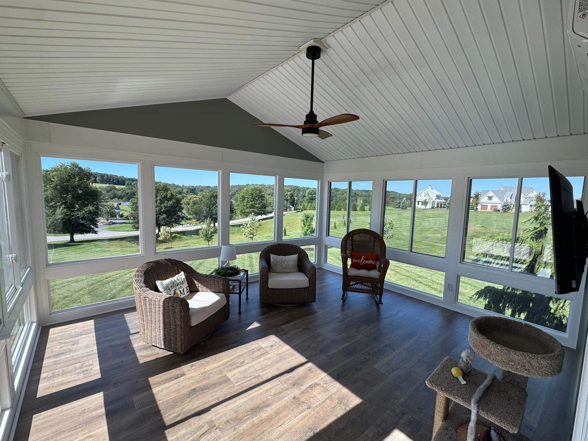 Sunroom interior with a vaulted white ceiling, ceiling fan, and wicker chairs facing windows over open countryside