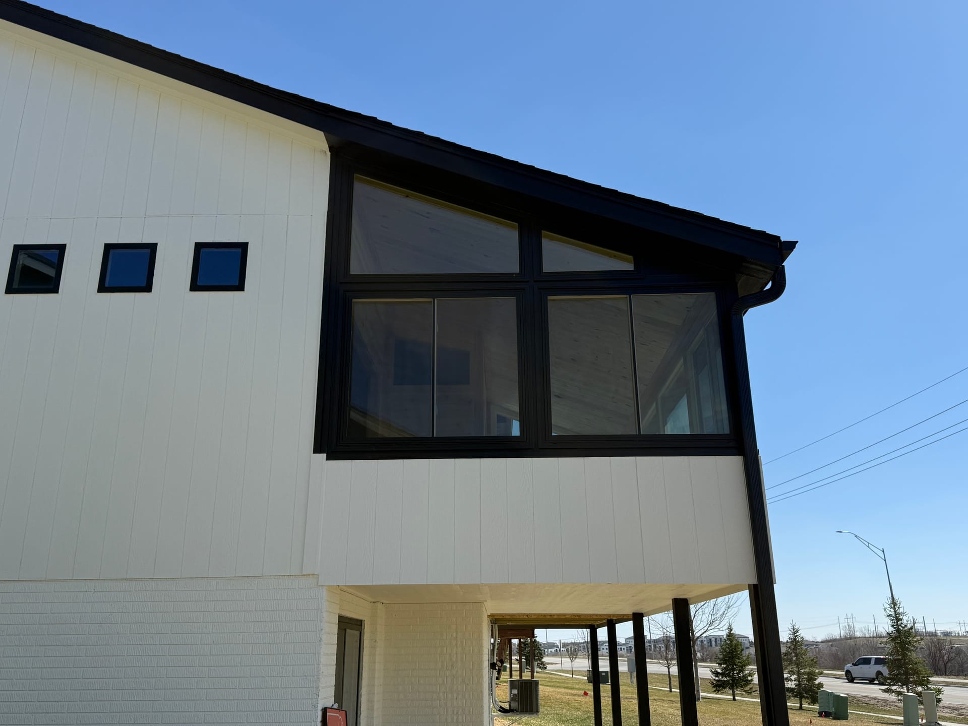 Second-story sunroom with black-framed windows on a modern white home