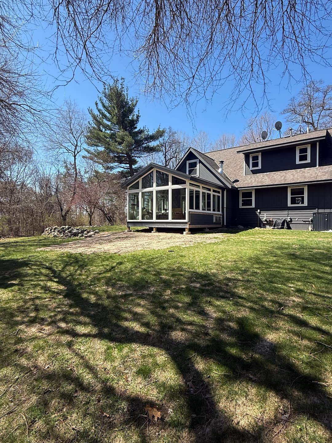 Gable-roof sunroom addition on a navy home, seen across a spring backyard