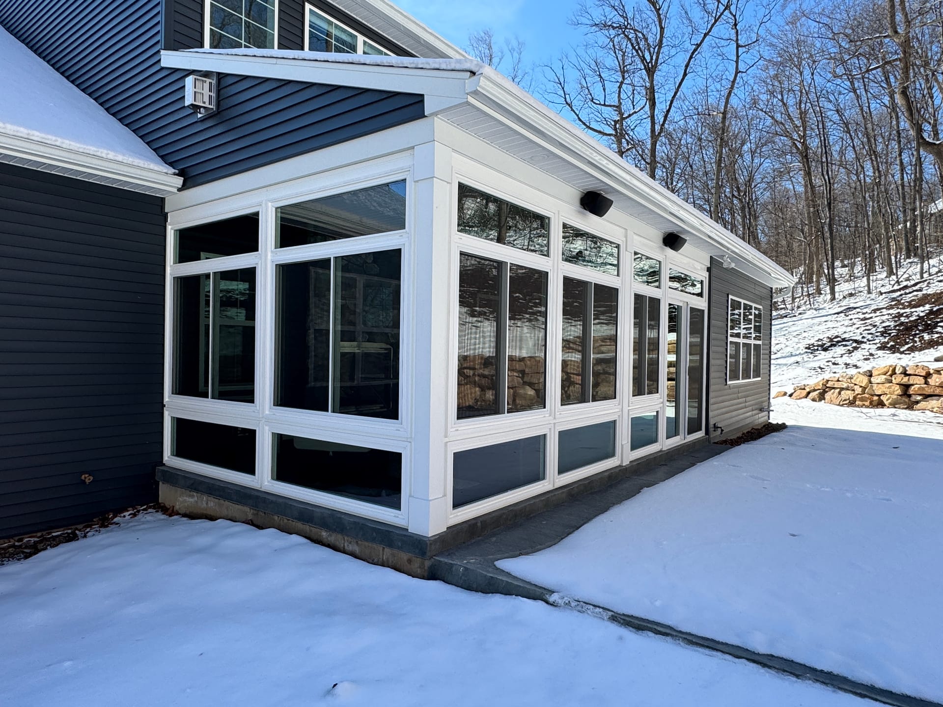 White-framed sunroom addition on a navy-sided home after a winter snowfall